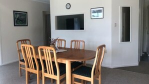 A dining area with a round wooden table and six chairs, a clock on the wall, and a framed picture. - Private Island Eco Retreat complete with resident Kiwi (Kerikeri)