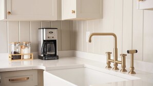 A kitchen with white cabinets, a coffee maker, and a gold faucet. - Historic Cottage in Perry - 3 Bedroom 2 Bath (Perry)