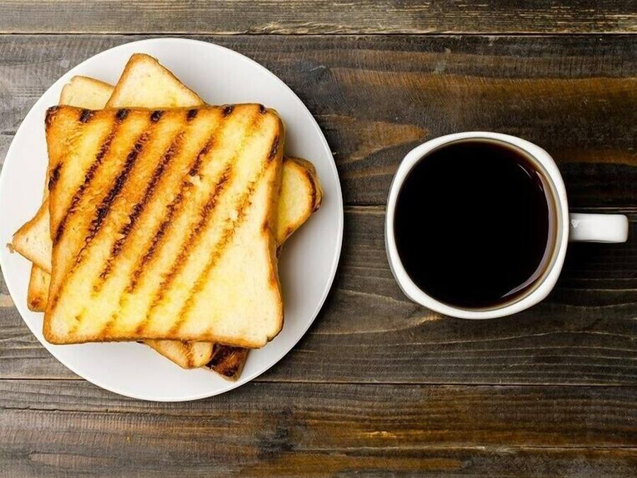 Een bord gegrilde kaassandwiches en een kop zwarte koffie op een houten tafel.