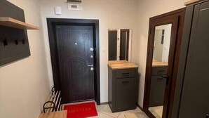 Un pasillo estrecho con un banco de madera, un mueble pequeño, un espejo y una puerta con un diseño decorativo.