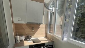 Cocina pequeña con ventana, un lavabo, una hornilla y una silla.