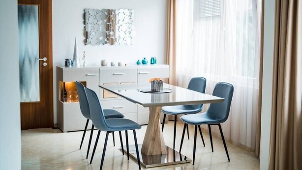 Ein moderner Essbereich mit einem rechteckigen Tisch, vier blauen Stühlen und einer weißen Kommode mit Schubladen.