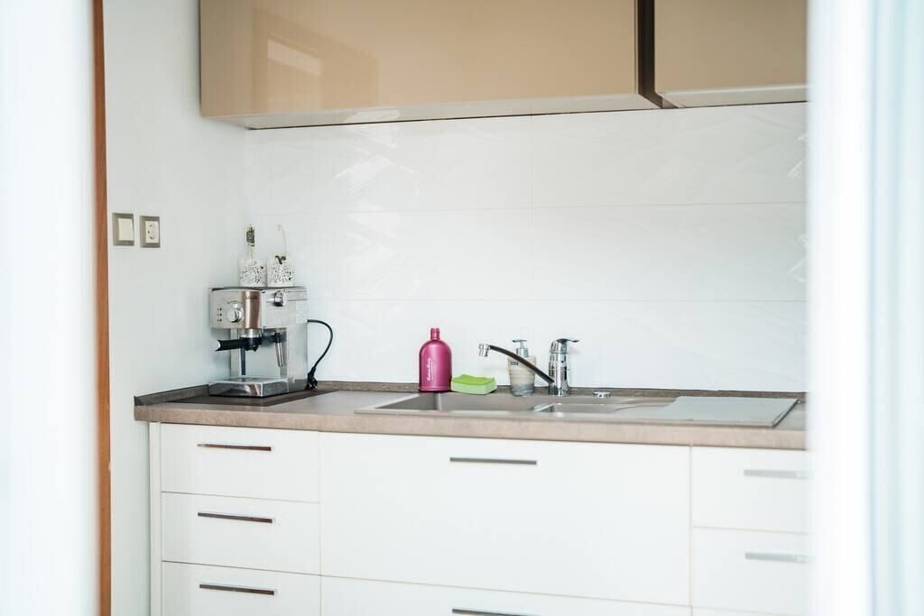 A modern kitchen with white cabinets, a stainless steel coffee maker, a pink bottle, and a green dish soap.