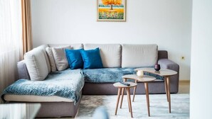 Ein modernes Wohnzimmer mit einem Ecksofa, einem kleinen Couchtisch und einem Baumgemälde an der Wand.