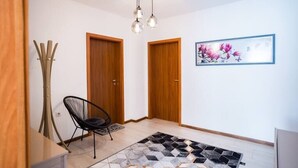 Ein Flur mit einem schwarzen Stuhl, Holztüren, einem gemusterten Teppich und einem gerahmten Blumenbild an der Wand.