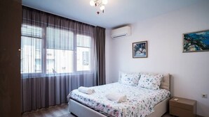 Ein Schlafzimmer mit einem Bett, Vorhängen, einer Klimaanlage, einem Nachttisch und einem Bild an der Wand.
