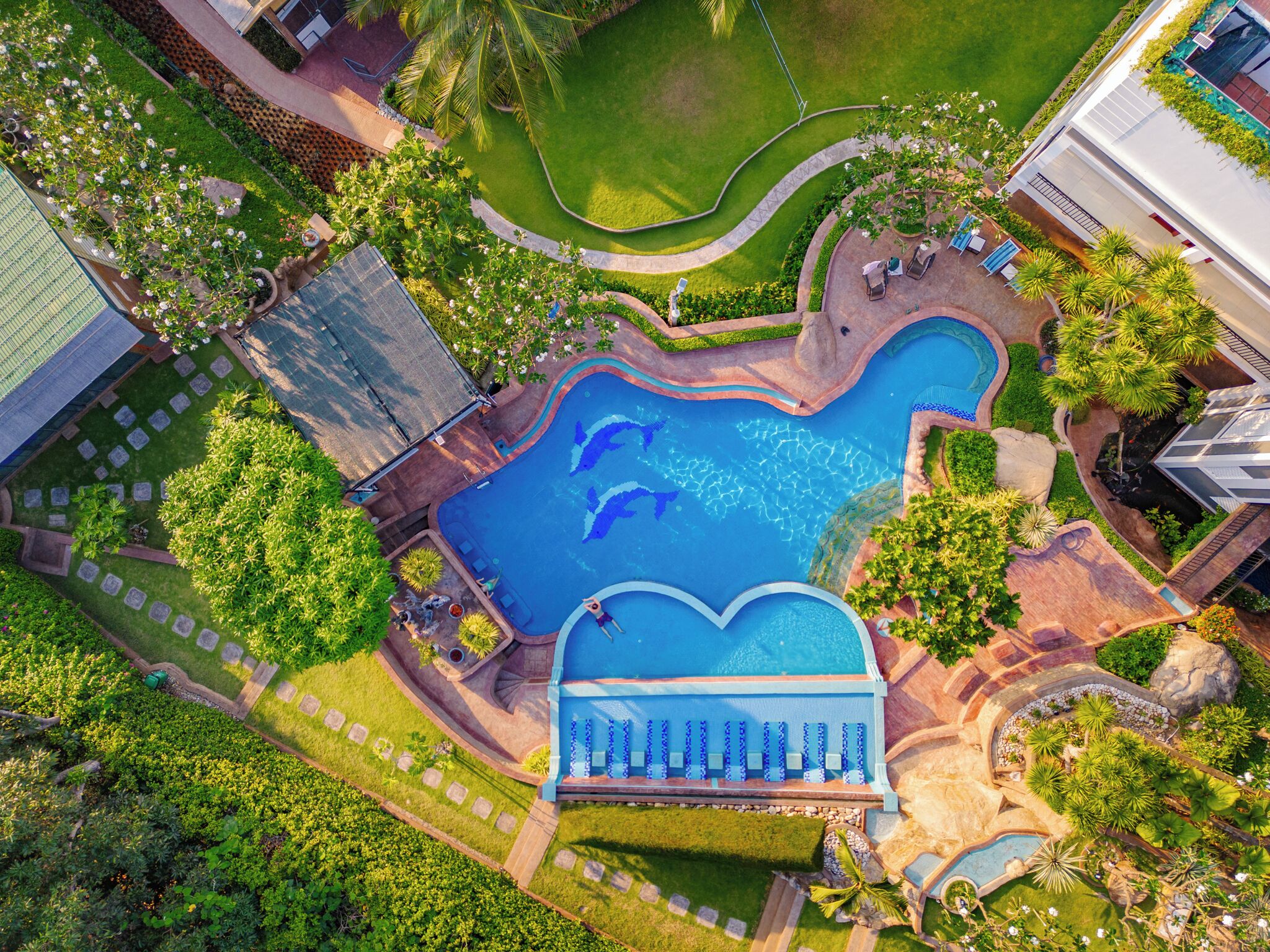 An aerial view of a resort with a heart-shaped pool, surrounded by lush greenery and palm trees.