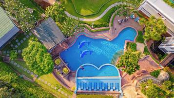 An aerial view of a resort with a heart-shaped pool, surrounded by lush greenery and palm trees.