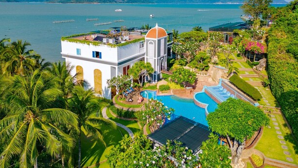 Um resort com piscina, palmeiras e vista para o mar.