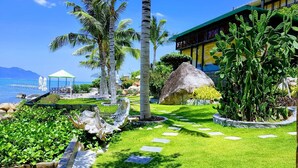 Um resort com uma cabana de telhado de palha, palmeiras e vista clara para o oceano.