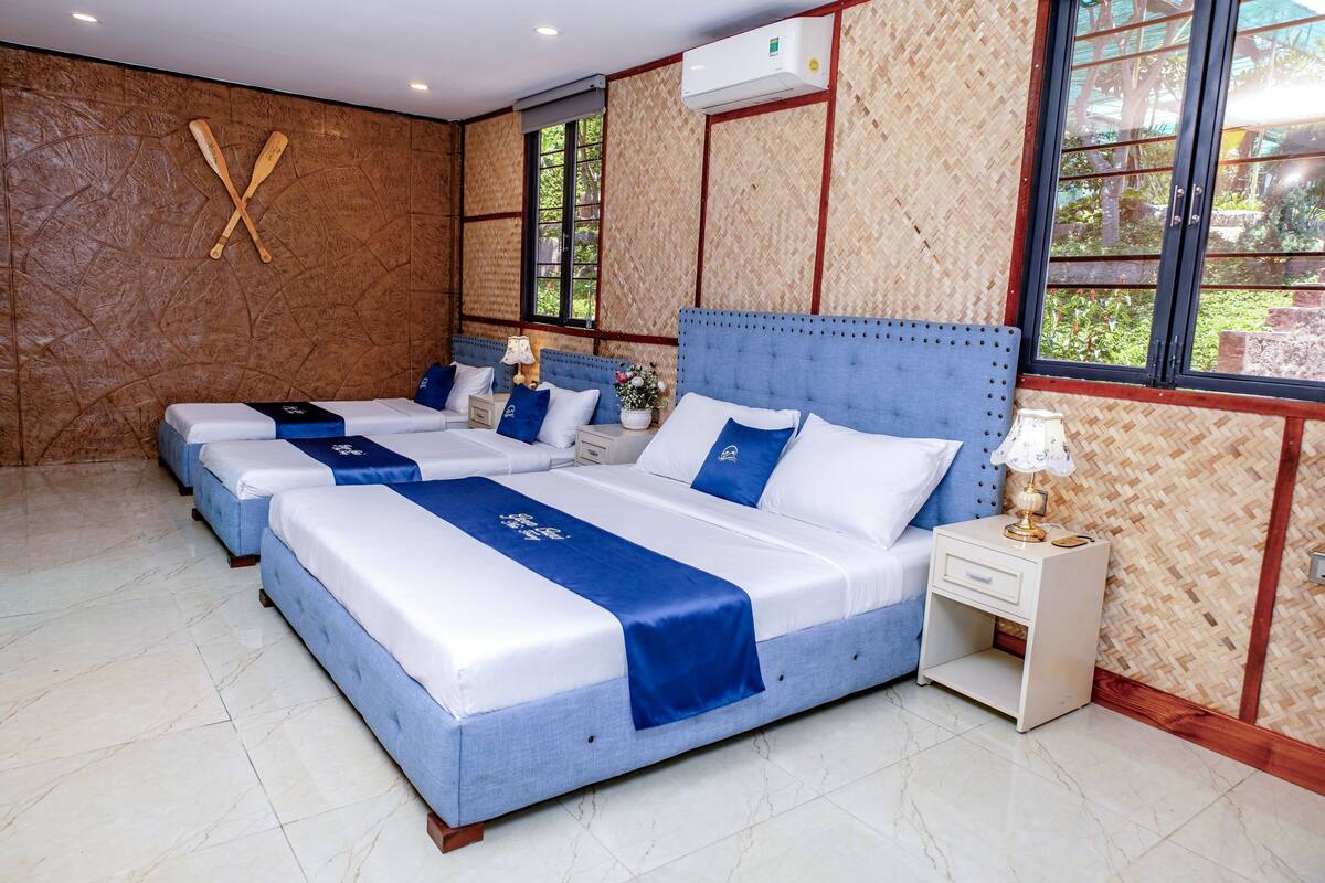 Een hotelkamer met drie bedden, een groot raam en een luchtverkoeler aan de muur.