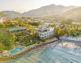 Un resort con piscina, playa y montañas al fondo.