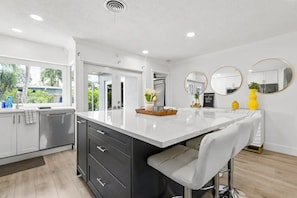 A modern kitchen with a large island, dark cabinets, and a view of the outdoors. - Tropical Oasis with Heated Pool and Cabana Bar (Oakland Park)