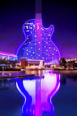 A building with a guitar-shaped neon light design, a pool, and a reflection of the guitar in the water. - Tropical Oasis with Heated Pool and Cabana Bar (Oakland Park)