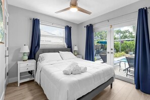 A bedroom with a bed, bedside tables, a ceiling fan, and a view of an outdoor patio with a table and chairs. - Tropical Oasis with Heated Pool and Cabana Bar (Oakland Park)