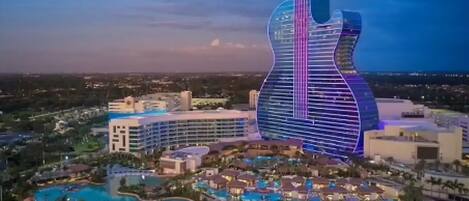 A large resort with a distinctive guitar-shaped building, multiple swimming pools, and surrounding villas.
