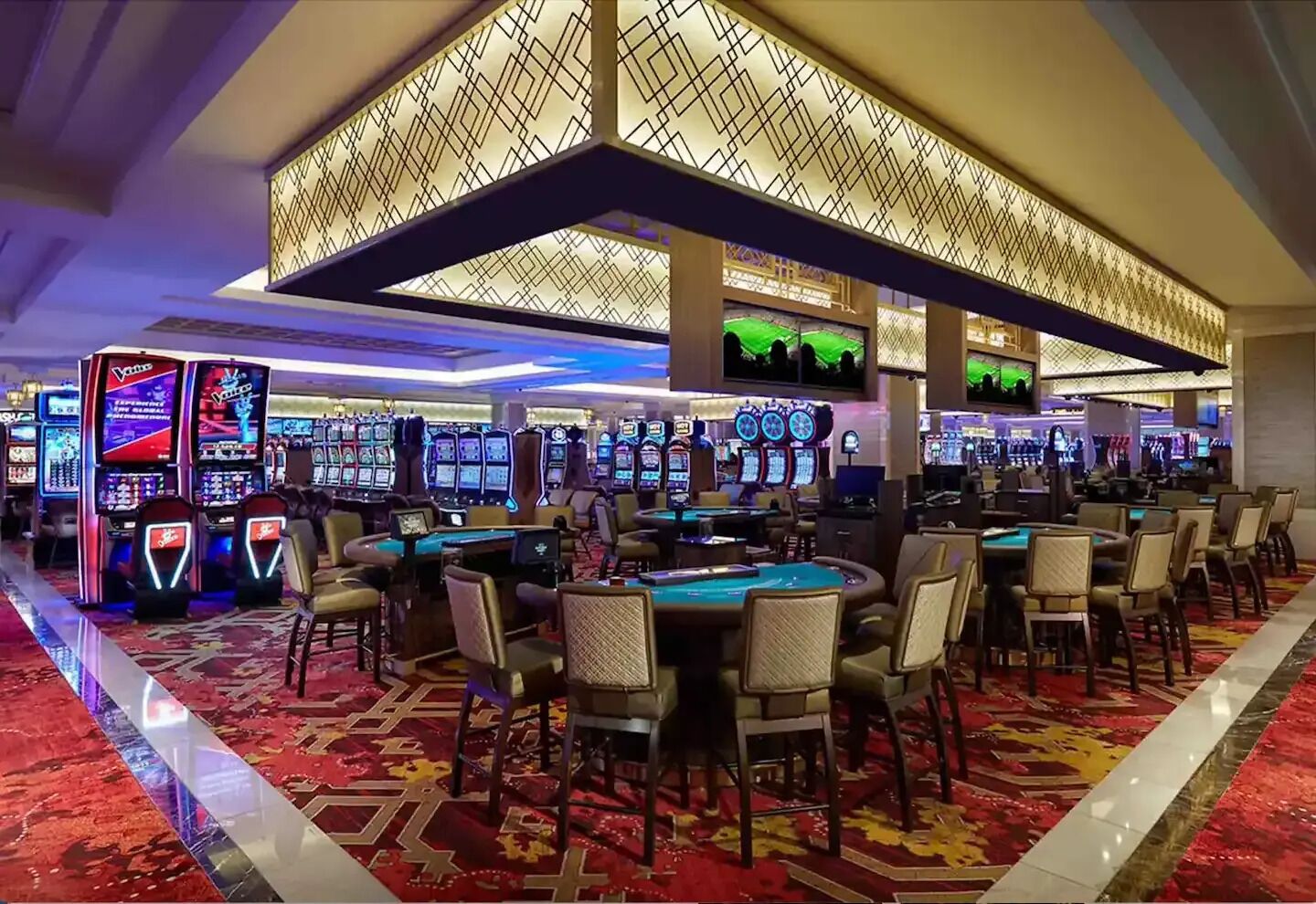 Ein Casino mit zahlreichen Spielautomaten, Blackjack-Tischen und einer großen, gemusterten Decke.