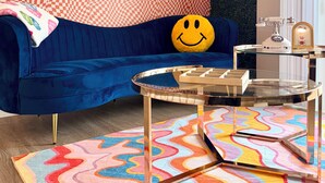 Una sala de estar moderna con un sofá azul, una mesa de centro de cristal y una alfombra colorida.