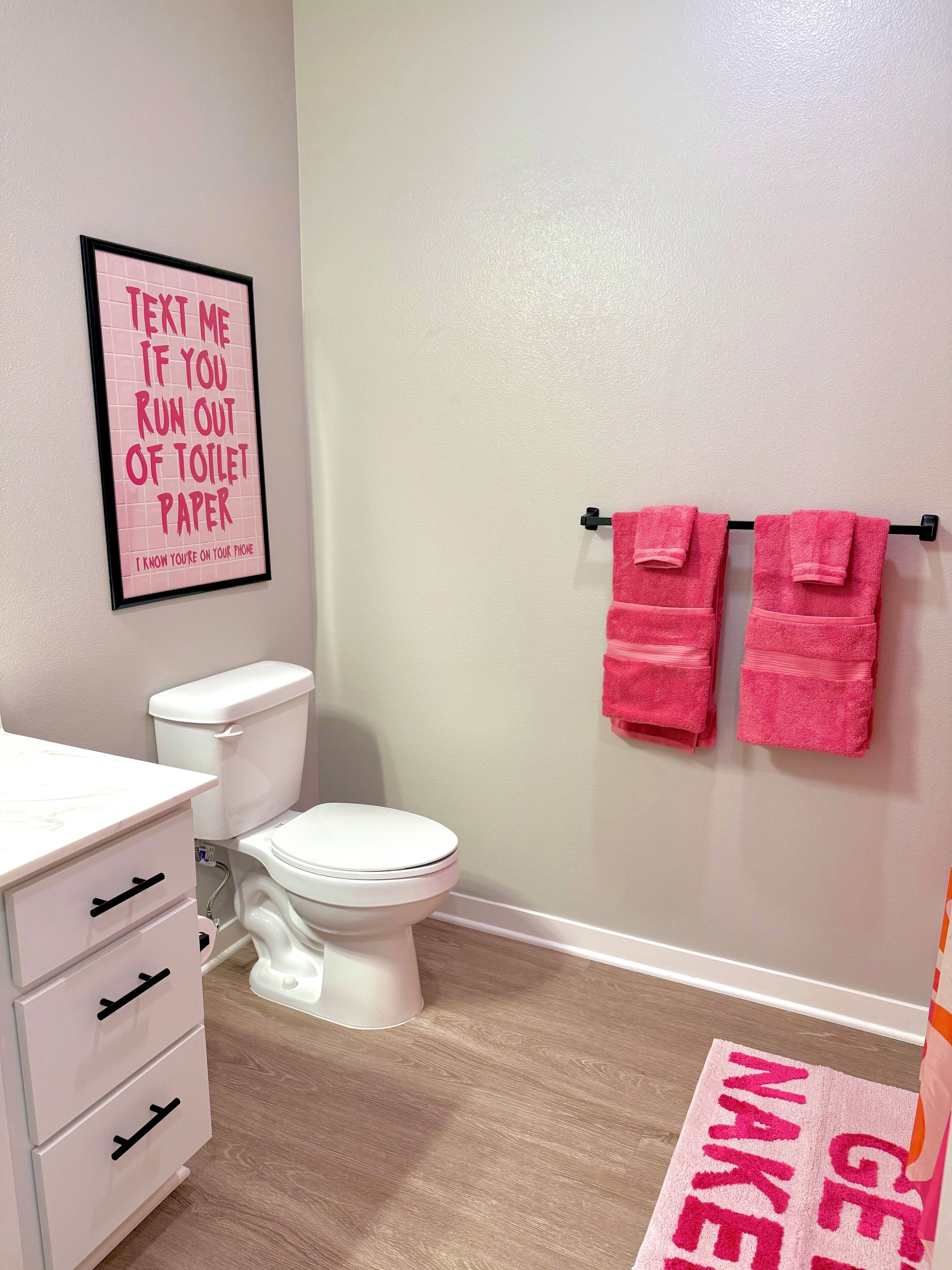 A bathroom with a toilet, a sink with a mirror, and a pink towel rack.