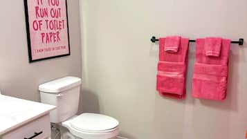 A bathroom with a toilet, a sink with a mirror, and a pink towel rack.