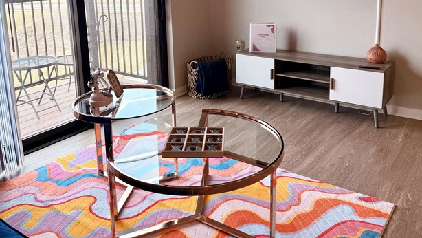 Una sala de estar moderna con una mesa de centro de vidrio, un sofá, un televisor y vistas al exterior.