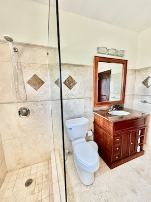 A bathroom with a shower, toilet, and vanity with a mirror. - West End Bay Condos (West End Village)