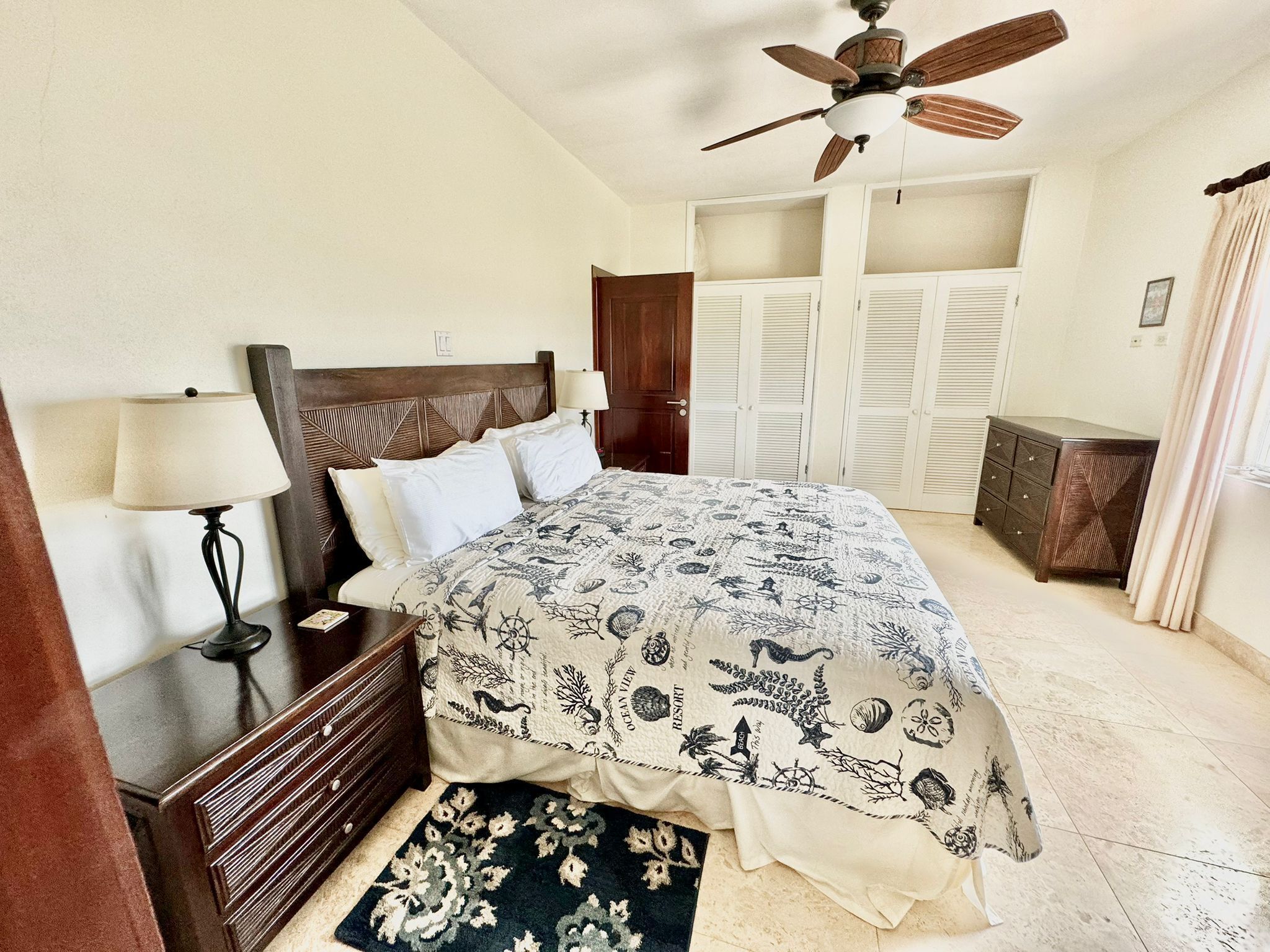 A bedroom with a bed, a nightstand, a dresser, a ceiling fan, and a wardrobe.