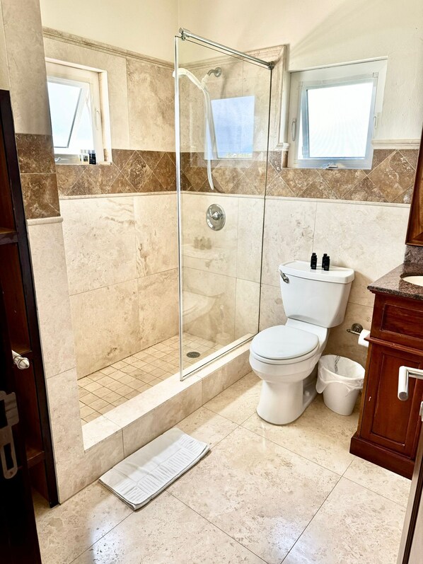 A bathroom with a glass-enclosed shower, a toilet, and a sink. - West End Bay Condos (West End Village)