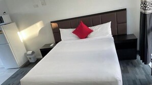 A neatly made bed with a red pillow, a bedside table, and a nightstand. - Krishna Motel (Papakura)