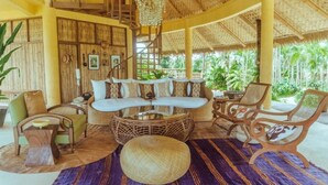 A spacious lounge with a thatched roof, wicker furniture, and a view of palm trees. - INARA Siargao (General Luna)