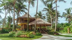A thatched-roof house with a balcony, surrounded by palm trees and lush greenery. - INARA Siargao (General Luna)