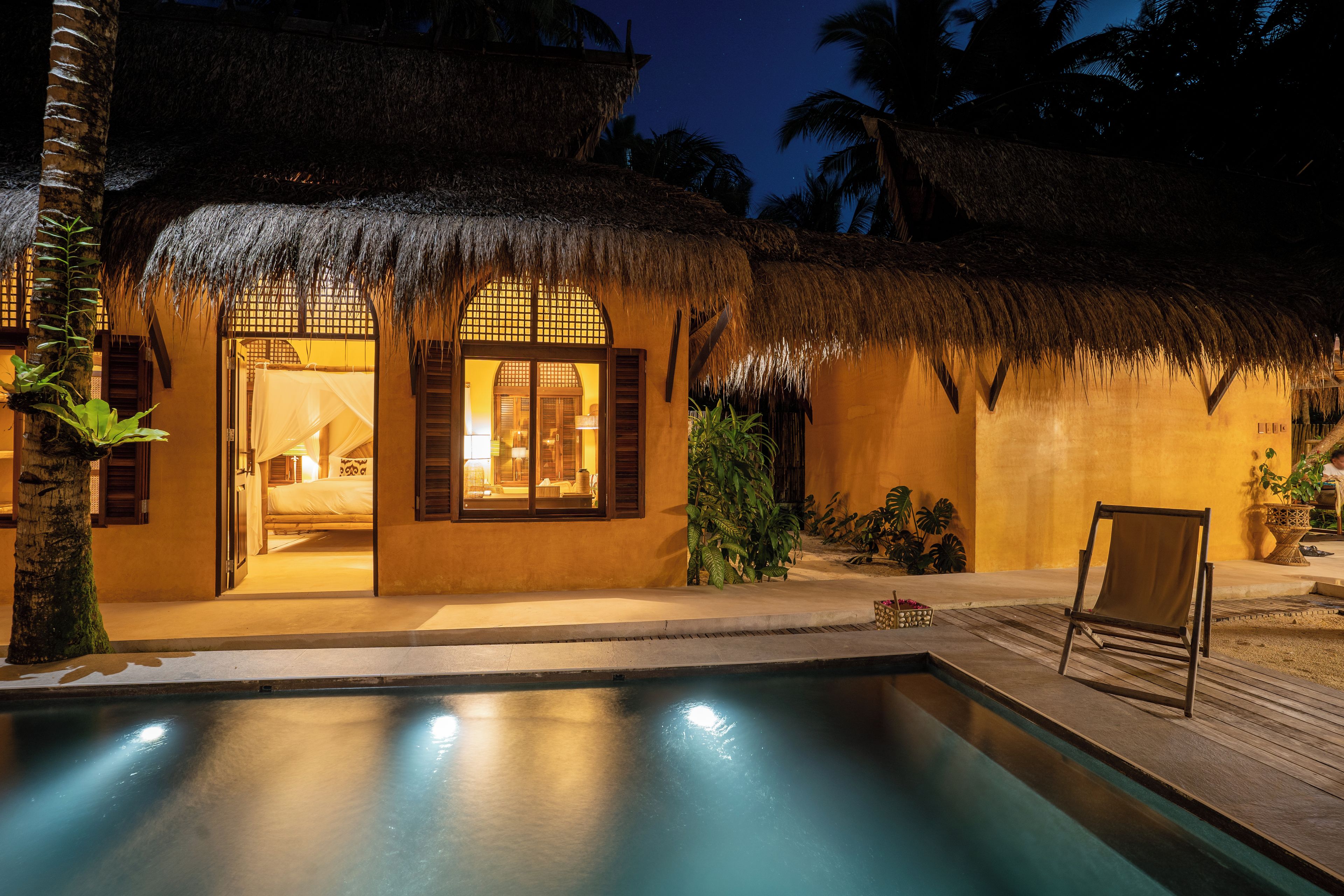 A resort with a pool, thatched-roof buildings, and tropical plants.