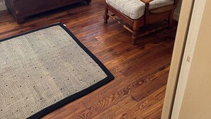A cozy room with a wooden floor, a patterned rug, a wooden coffee table with decorative items, a striped armchair, and a window with blinds.