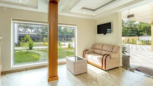 A spacious room with a large window, a sofa, a coffee table, and a flat-screen TV mounted on the wall. - ESAA Airport Hotel (Aluva)