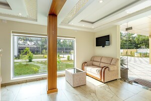 A spacious room with a large window, a sofa, a coffee table, and a flat-screen TV mounted on the wall.