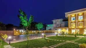 A courtyard with a paved walkway, a well-maintained lawn, and a building with multiple windows and balconies. - ESAA Airport Hotel (Aluva)