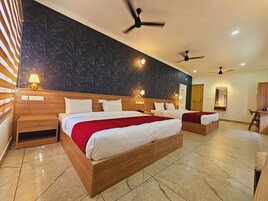 A hotel room with two beds, wooden headboards, marble flooring, ceiling fans, and wall-mounted lights.