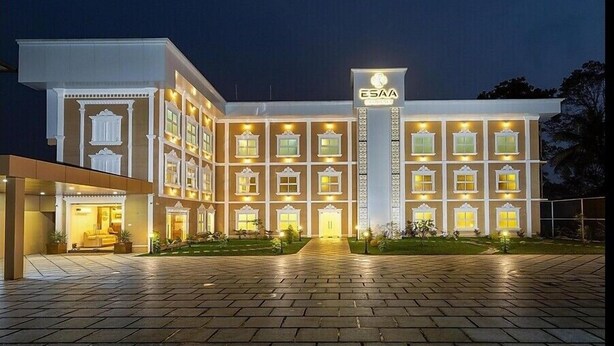 A multi-story hotel with a central entrance, illuminated windows, and a sign reading "ESAA". - ESAA Airport Hotel (Aluva)