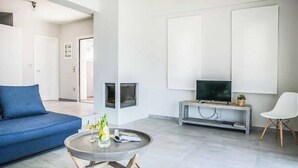 Un salon moderne avec un canapé bleu, une table basse ronde sur laquelle repose un magazine, un téléviseur à écran plat posé sur une console grise et un fauteuil blanc.