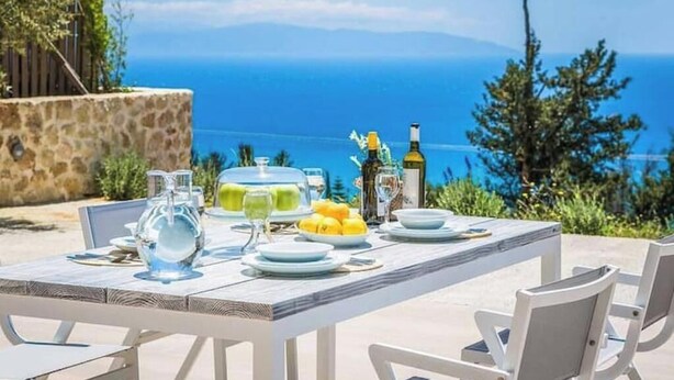 Une table dressée à l’extérieur, avec vue sur la mer, un mur en pierre et de la verdure.