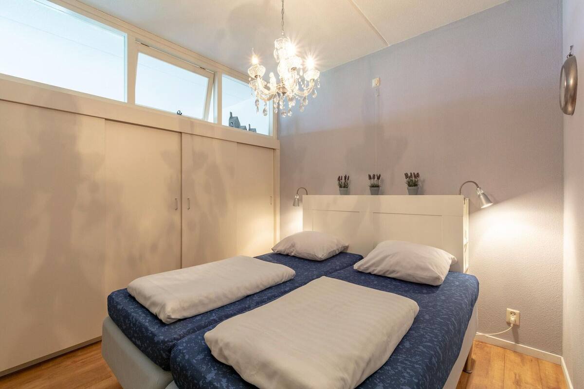 A bedroom with a bed, a chandelier, a window, and a wall-mounted shelf with plants.