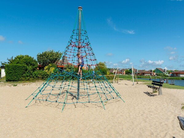 A playground with a climbing structure and a bench near a body of water. - An Apartment That is Attractively Furnished (Julianadorp)