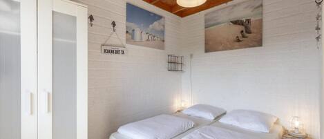 Un dormitorio con dos camas, paredes blancas, vigas de madera en el techo y un armario blanco.