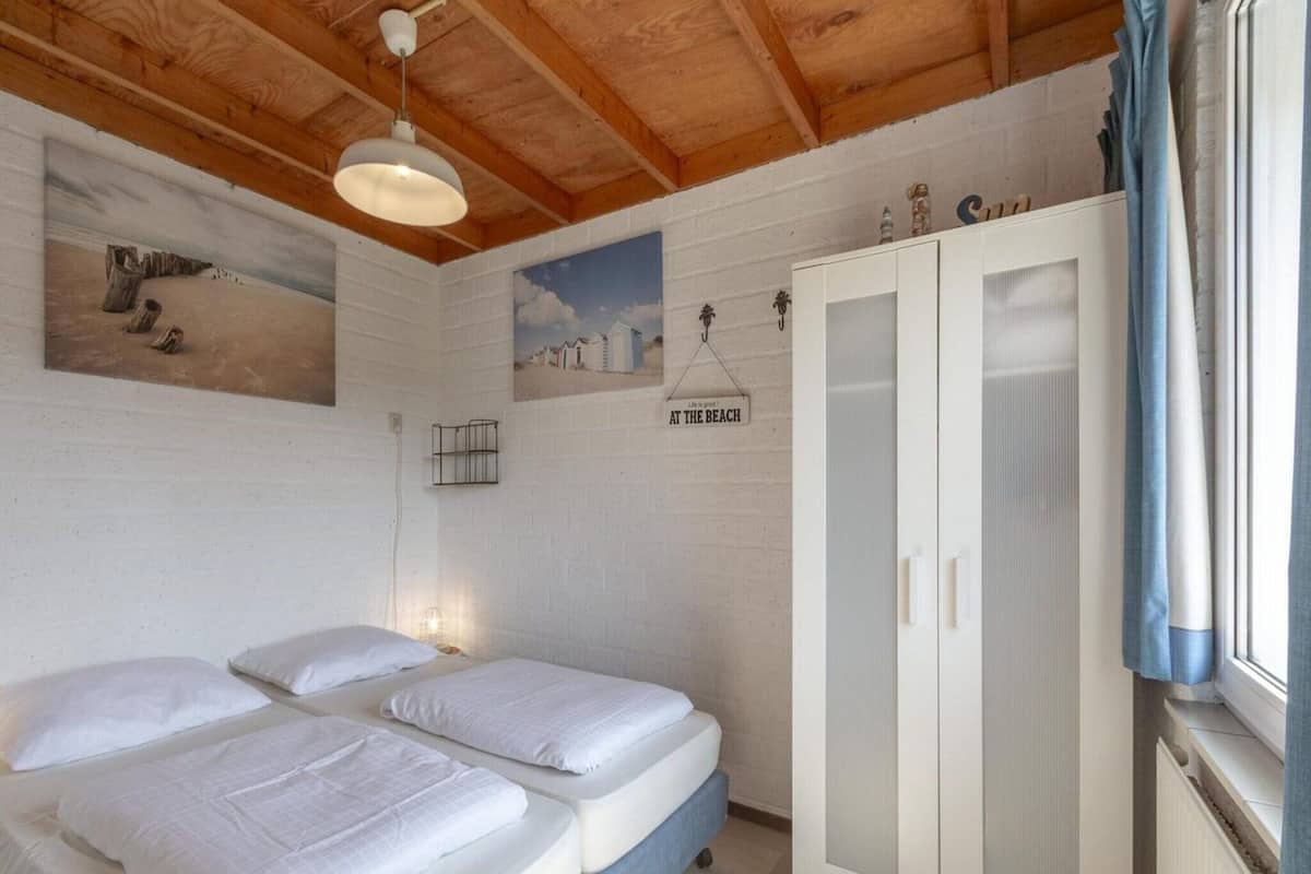 A bedroom with two beds, a wardrobe, a painting of a beach scene, and a sign that says "Life is good! AT THE BEACH".