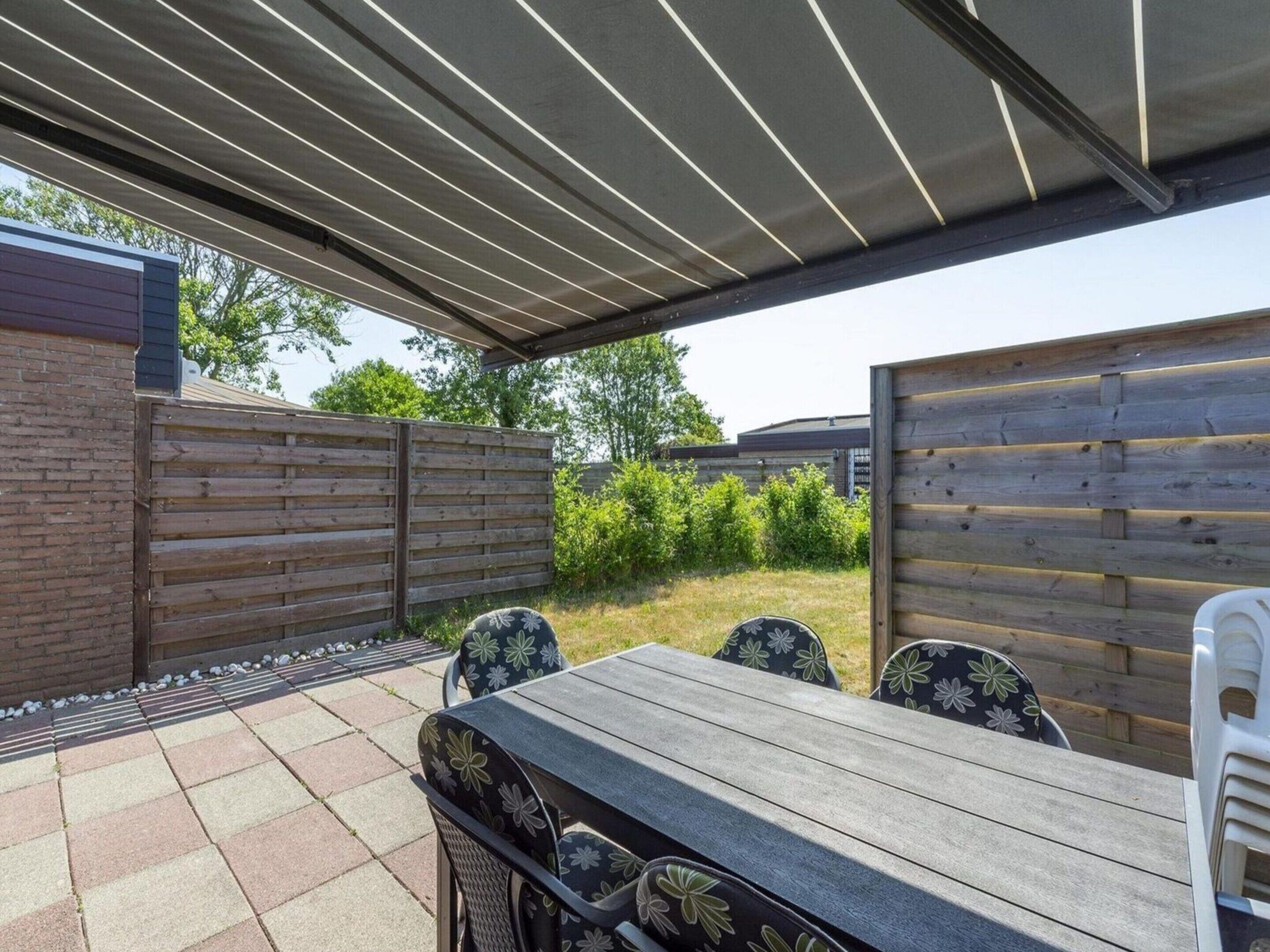 Une terrasse extérieure avec une table et des chaises en bois, un espace abrité et un mur en briques.
