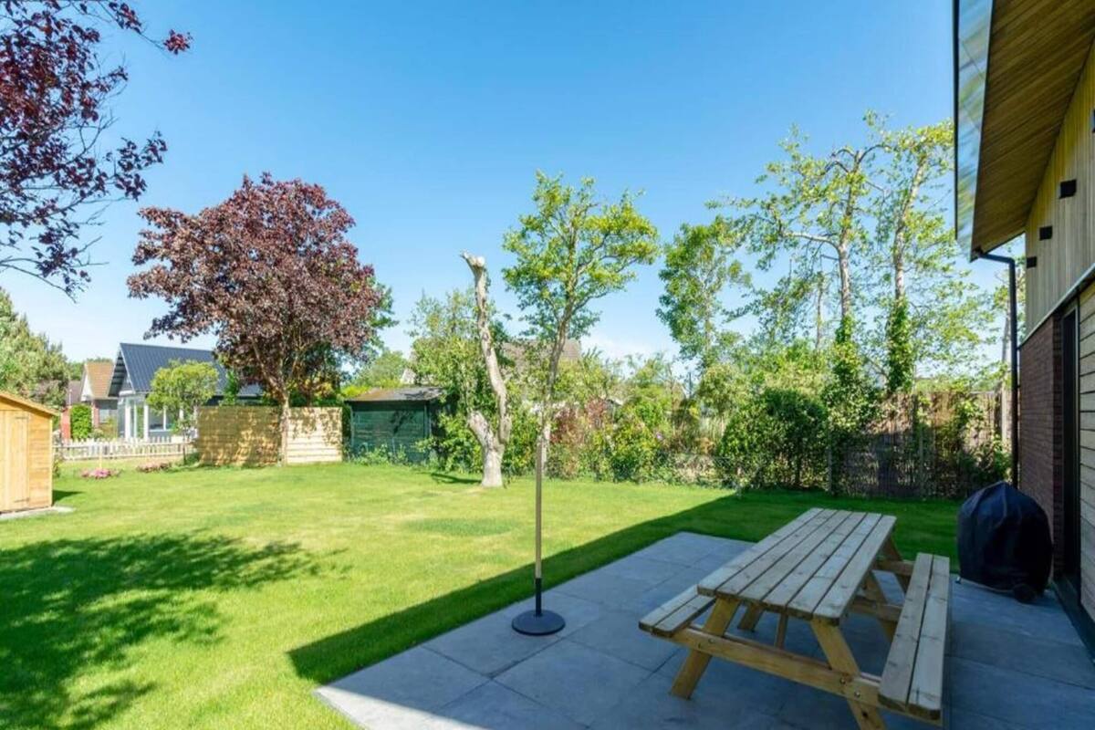 Ein Garten mit einem Holztisch, einem Steinweg und verschiedenen Bäumen und Sträuchern.