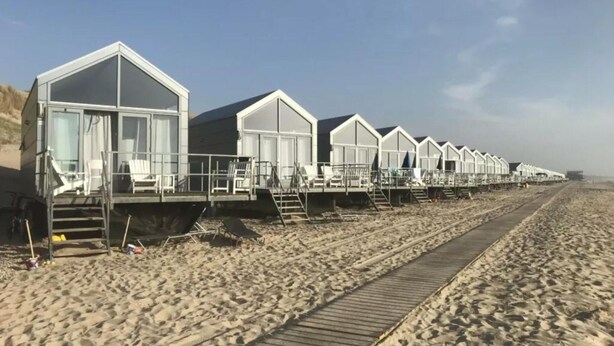 A row of beach huts with steps leading up to them, a wooden boardwalk, and a sandy beach. - a Nice Holiday by the sea With Family (Julianadorp)