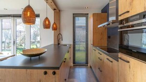 A modern kitchen with wooden cabinets, a large island, hanging pendant lights, and a built-in oven. - a Nice Holiday by the sea With Family (Julianadorp)