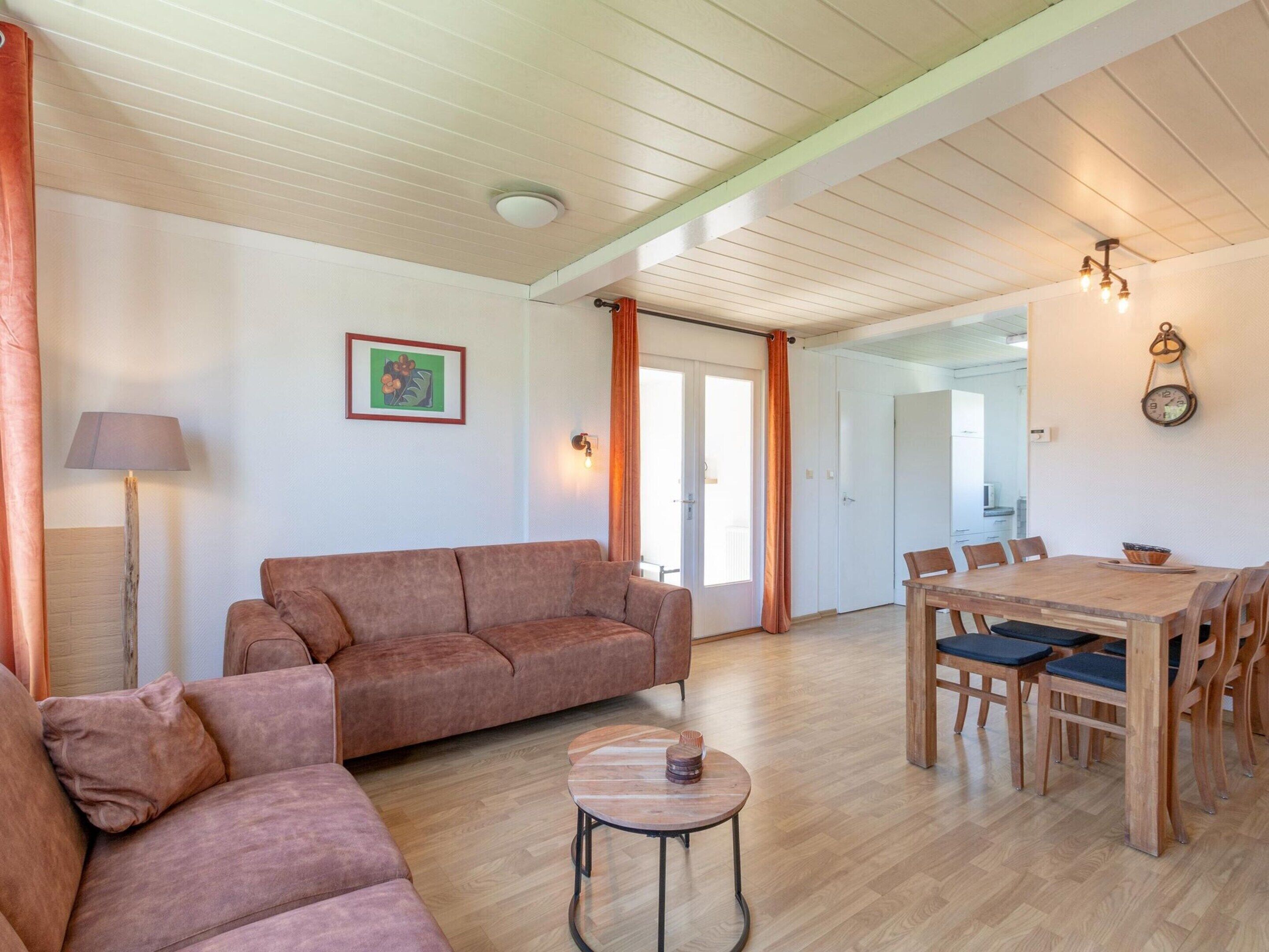 A spacious living area with a wooden floor, a brown sofa, a round coffee table, and a dining table with chairs.