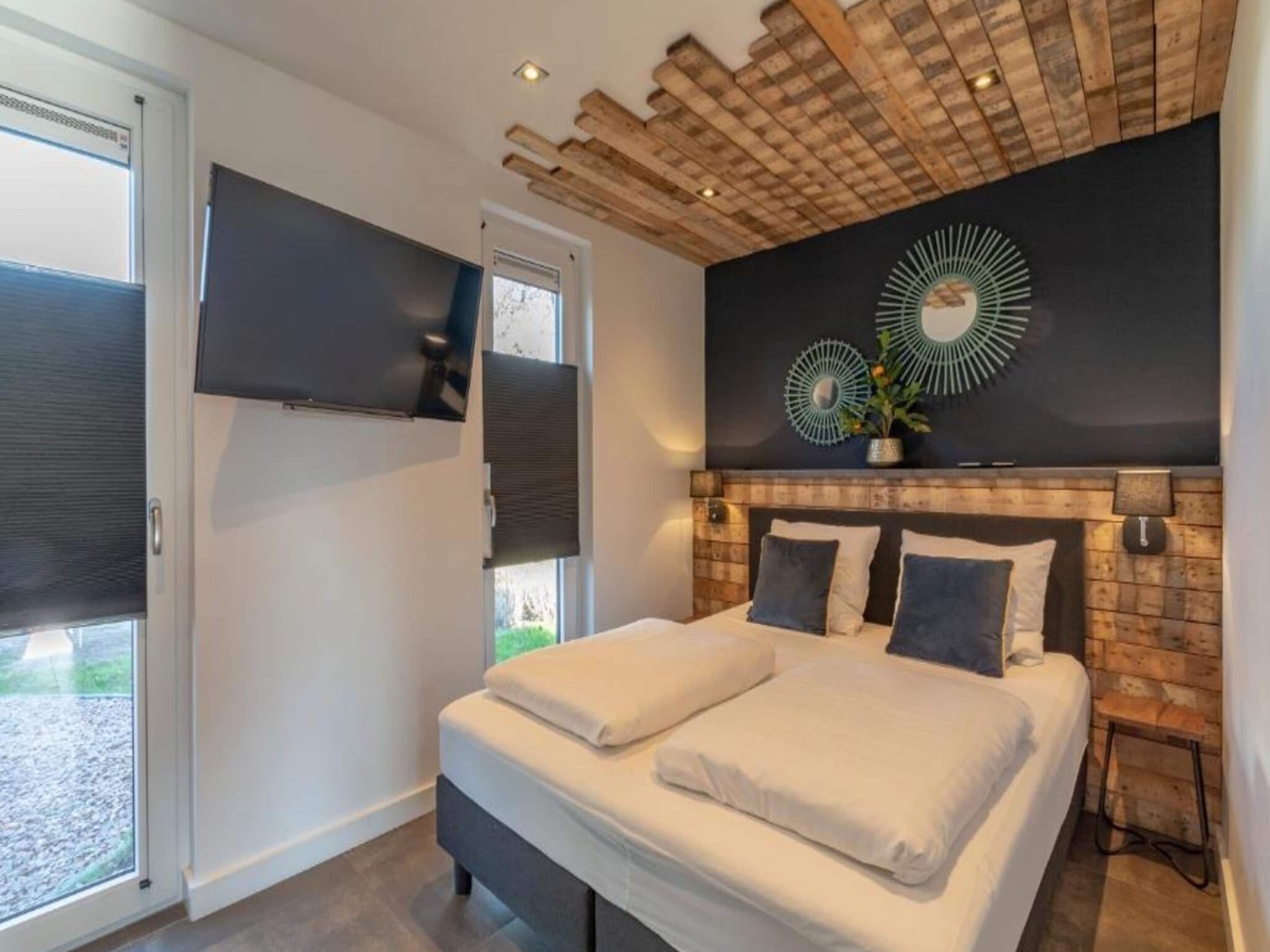A modern bedroom with a large bed, a TV mounted on the wall, and a unique ceiling design.